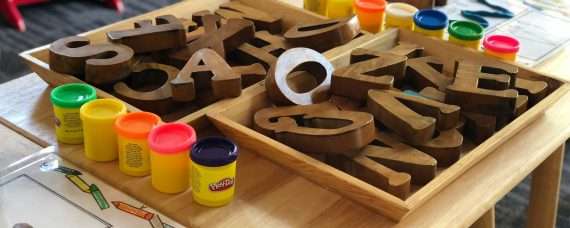 A table set up for a children's activity with trays of brown wooden alphabet letters and Play-Doh cups of different colors